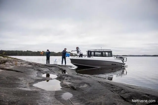 Men unload equipment from a boat on rocky shore, with a calm lake and forested landscape in the background.